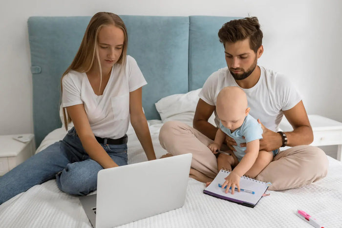 Parents faisant le point sur leur budget bébé, assis sur un lit avec leur enfant